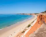 Blick auf den Strand Praia da Falésia mit seinen roten Felsen und der Stadt im Hintergrund.