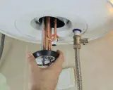 Mano ajustando la resistencia termoeléctrica de un calentador de agua.