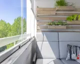 Przytulny balkon w bloku z szarą kanapą, poduszką z liskiem i zielenią na drewnianej ściance.