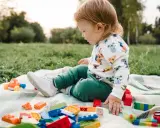 Un niño pequeño juega con bloques de construcción y un coche de juguete en el césped, disfrutando de actividades para niños de 2 a 3 años.