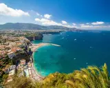 Vista panoramica della costa con il **scoglio del cavaliere** che emerge dal mare turchese, spiagge affollate e case aggrappate alla scogliera.