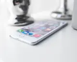 Biały iPhone leży na białym blacie, gotowy do pracy. W tle widać błyszczące i matowe elementy dekoracyjne.