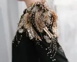 A black garment with an elaborate shoulder embellishment of gold and silver beads, sequins, and crystals, showcasing the definition of embellished fashion.