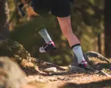 Beine einer Person beim **trail running** auf einem steinigen Waldweg. Leichte Sportschuhe und helle Socken mit Logo.
