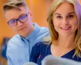 Uśmiechnięta studentka i jej koledzy analizują materiały. Akademia Leona Koźmińskiego czesne to inwestycja w przyszłość.