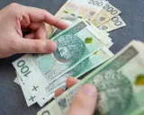 Dłonie liczą polskie banknoty 100 zł i 200 zł, przygotowując się do wypłaty świadczeń.