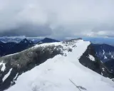Snöklädda bergstoppar och molniga himlar. En repstump syns i förgrunden, redo för äventyret på Kebnekaise leder.