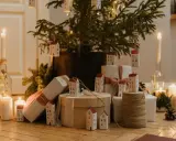 Julkalender tips: En julgran med små hus som dekorationer, presenter och ljus skapar en mysig julstämning.