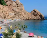 Playa de arena gris con gente disfrutando del sol y el mar, rodeada de acantilados. Un paraíso entre los pueblos de Granada con playa.