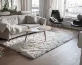 En fluffig, vit matta ligger framför en ljusgrå soffa och skapar en mysig känsla i vardagsrummet.