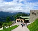 Besucher erkunden das Dokumentationszentrum Obersalzberg, umgeben von grünen Hügeln und Bergen.
