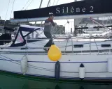 Un homme ajuste un pare-battage jaune sur un voilier. Ces bouées protègent la coque des chocs.