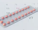 Różne rodzaje tabletek antykoncepcyjnych w blistrze na tle kalendarza.