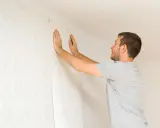 Hombre colocando papel pintado con patrón floral en una pared. Aprende como poner papel pintado tú mismo.