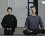 Två personer sitter på en yogamatta och mediterar. En kvinna i svart tröja och en man i grå tröja. Ta ett ögonblick att stanna upp.