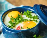 Un délicieux oeuf cocotte, parsemé de persil frais, prêt à être dégusté avec une fourchette.