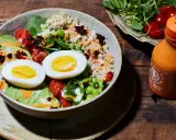 Gesunde Bowl-Ideen: Quinoa, Avocado, Ei, Edamame und Kirschtomaten, beträufelt mit Sriracha-Mayo.