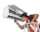 Un technicien vérifie un climatiseur mobile qui ne refroidit plus. Il est sur une échelle, examinant l'appareil.