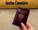 Dłoń trzyma polski paszport na tle tablicy z napisem "Section Consulaire".