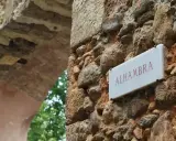 Schild "Alhambra" an einer alten Steinmauer, die zu einem Parkplatz führt.
