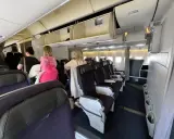 Wnętrze samolotu z rzędami foteli i pasażerami w przejściu.