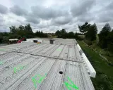 Budowa domu w toku. Widok na strop z prefabrykatów, zbrojenie czeka na beton. W tle drzewa i pochmurne niebo.
