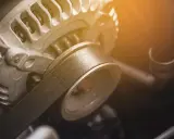 Zbliżenie na spalony alternator samochodowy z widocznym paskiem klinowym.