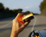 Mano sujeta una baliza de emergencia naranja brillante, lista para evitar una multa o señalizar un peligro en la carretera.