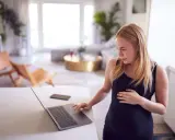 Ciężarna kobieta sprawdza na laptopie, czy skurcze co 20 minut oznaczają poród.