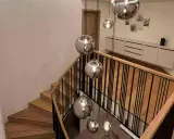 Nowoczesna klatka schodowa w domu z drewnianymi stopniami i czarną balustradą, ozdobiona wiszącymi, lustrzanymi kulami.