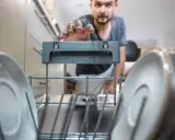 Mężczyzna próbuje uruchomić zmywarkę, która nie reaguje na przyciski. Wnętrze zmywarki z talerzami.