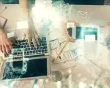 Dwie osoby pracują przy biurku, jedna pisze na laptopie, druga trzyma smartfon. Wokół latają ikony kopert, sugerując komunikację. Jak zacząć maila?