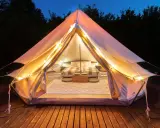 Mysig glamping i Sverige. Ett upplyst tält med säng och mysig inredning på en träaltan, omgivet av mörka träd.