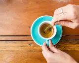 Mani che mescolano un caffè, nonostante si dica che il caffè è cancerogeno, il suo aroma attira.