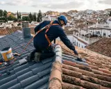 Trabajador realiza impermeabilización de tejados con equipo de seguridad, aplicando producto sobre tejas.