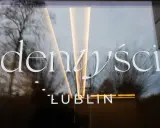 Napis "Dentyści Lublin" na szklanych drzwiach z odbiciem drzew i światła.