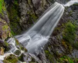 Vattenfall Storhogna forsar nerför en mossig klippvägg. Vattnet är silkeslent och omgivningen grönskande.
