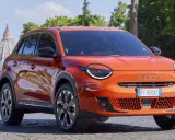 El nuevo Fiat 600, un SUV naranja vibrante, se exhibe con elegancia frente a la cúpula de San Pedro en Roma.
