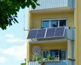 Två solceller monterade på en balkong på ett gult flerfamiljshus. Gröna växter i krukor på den nedre balkongen.
