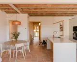 Comedor y cocina luminosos en una casa vieja decorada con poco dinero. Techos de vigas de madera y baldosas de terracota.