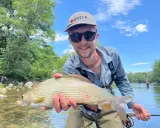 Glad fångst vid fly fishing. En man håller upp en fin fisk i en solig älv.