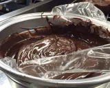 Ganache au chocolat, prête à refroidir au congélateur dans un bol en métal, recouverte d'une pellicule plastique.