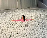 Mujer sonriente se sumerge en una piscina de bolas blancas, un divertido ikono madrid.