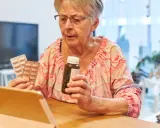 Starsza pani z tabletką w ręku sprawdza zwrot za leki dla seniorów.