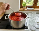 Łyżka nabiera gęsty, aromatyczny przecier pomidorowy z dużego garnka. Obok stoją czyste słoiki, gotowe do przetworów.