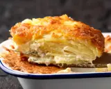 Une part généreuse de gratin de pomme de terre, avec sa croûte dorée et ses couches crémeuses, est soulevée par une spatule en bois.