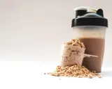 Ein Löffel Proteinpulver neben einem fertigen Proteinshake im Shaker. Perfekt für den proteinreichen Start in den Morgen.