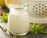 Ein Glas cremiges Ranch Dressing, daneben ein Schneebesen, Salatblätter und Zitronenspalten. Perfekt für dein Ranch Dressing Rezept!