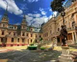 Pałac poznańskiego, z wieżyczkami i bogatymi zdobieniami, otoczony brukowanym dziedzińcem i zielenią.
