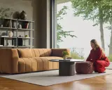 En kvinna i rött sitter på en pall bredvid en orange soffa. En dansk designer kan ha skapat detta stilrena vardagsrum.